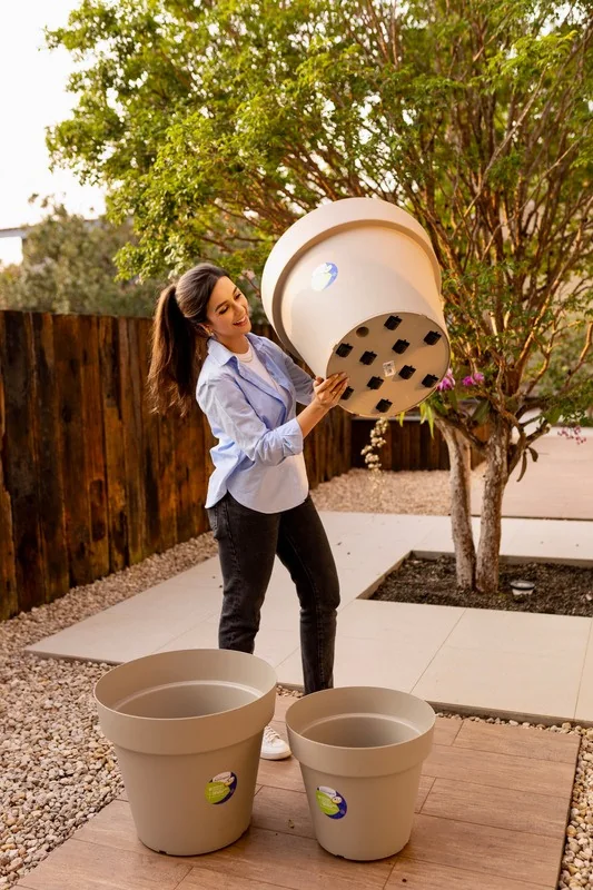 Mulher segurando um Vaso Bari grande em um jardim, com outros dois vasos no chão