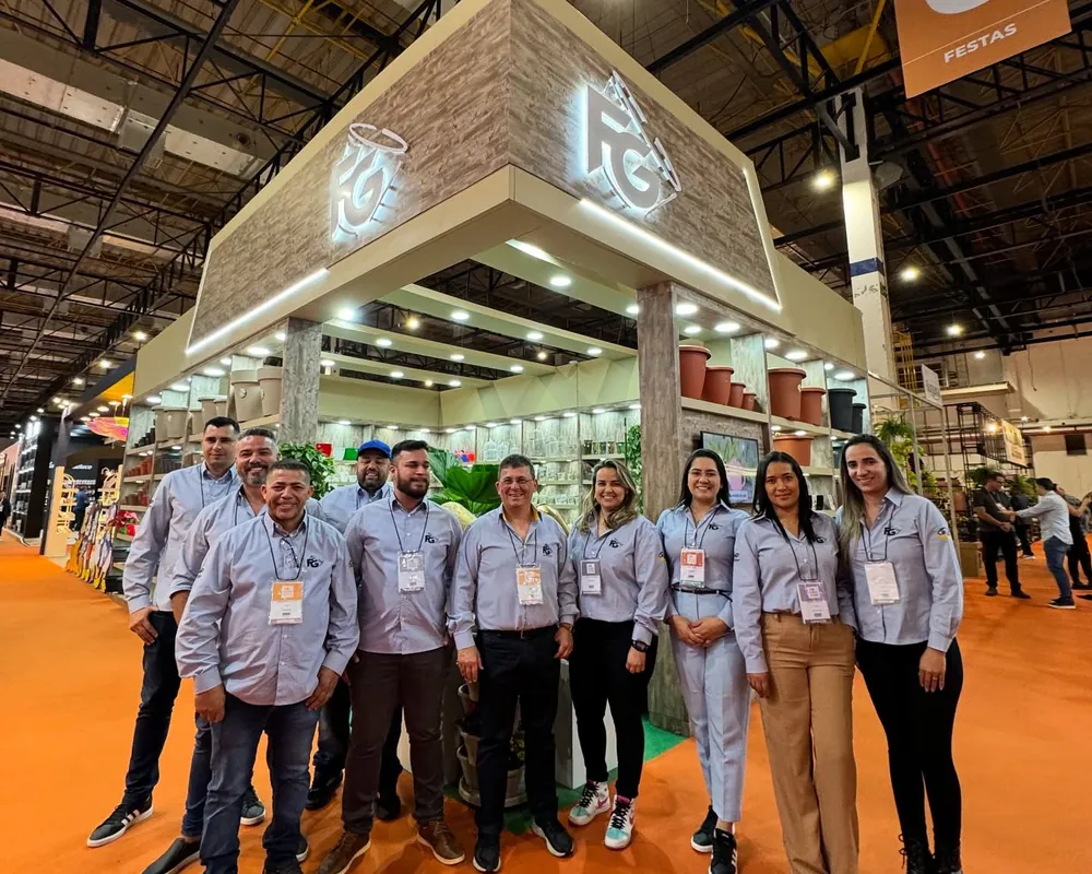 Time comercial da FG, de uniforme, em frente ao estande da empresa numa feira do setor