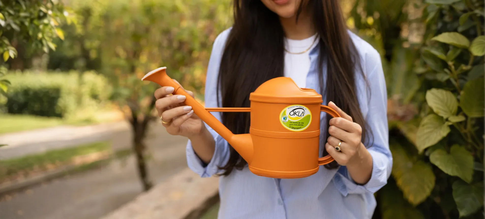 Mulher segurando um regador OKLA laranja em um jardim