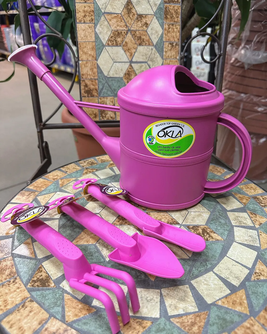 Regador OKLA rosa com um kit de pazinhas da mesma cor, sobre uma mesa de mosaico